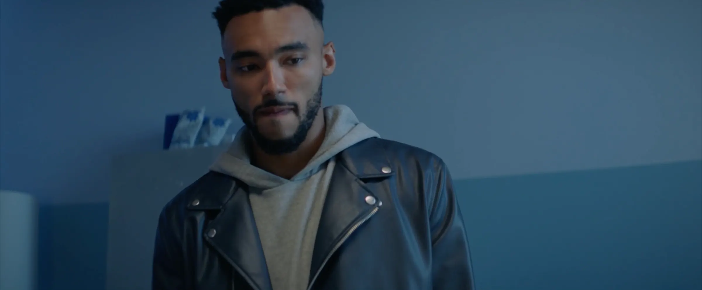 A young man in a leather jacket in a hospital corridor.